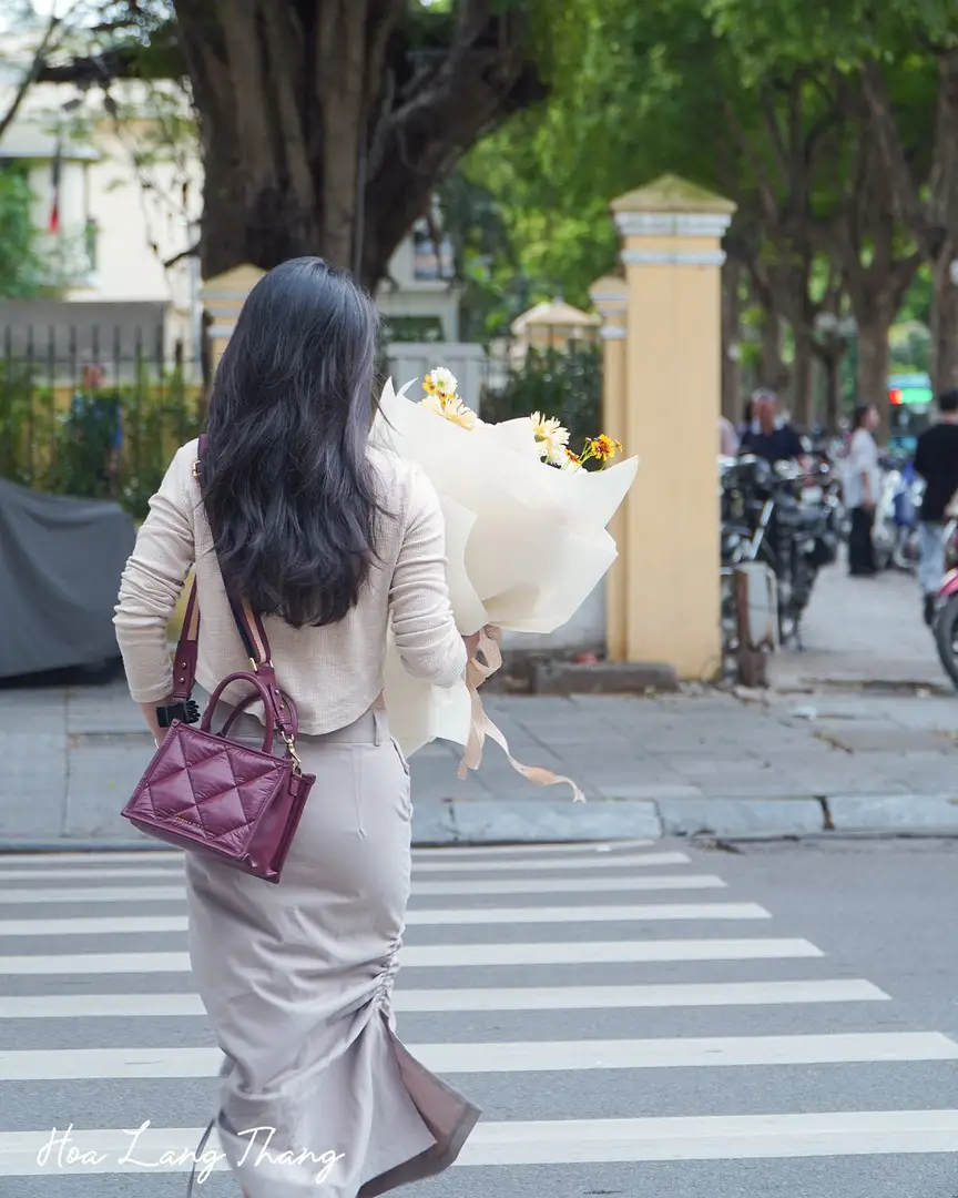 Người phụ nữ cầm bó hoa hướng dương và hoa hồng đi trên phố Hà Nội