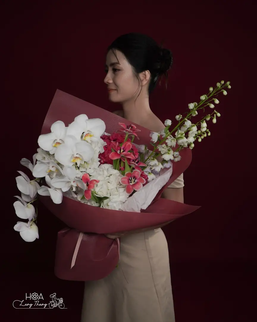 Người phụ nữ cầm bó hoa gồm lan hồ điệp, hồng, và hoa cúc, kiểu cắm sang trọng